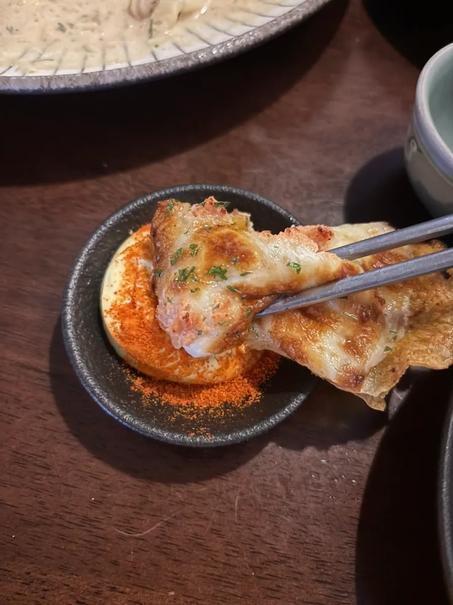 A piece of pollock roe cheese potato jeon dipped in sauce