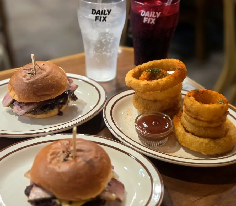 Table spread with two burgers, a heaping pile of onion rings, and soda in a branded cup