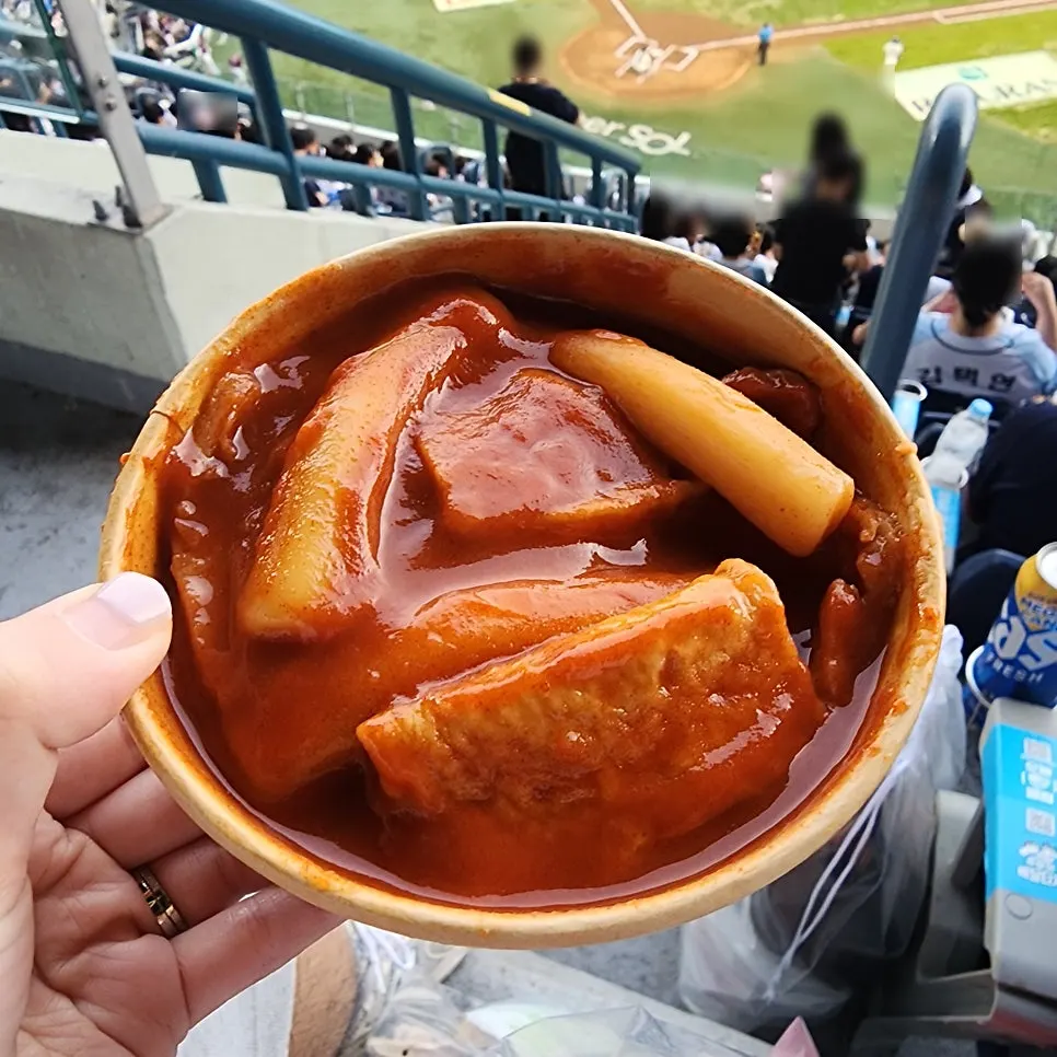 Paper cup of tteokbokki handed over at a stadium seat
