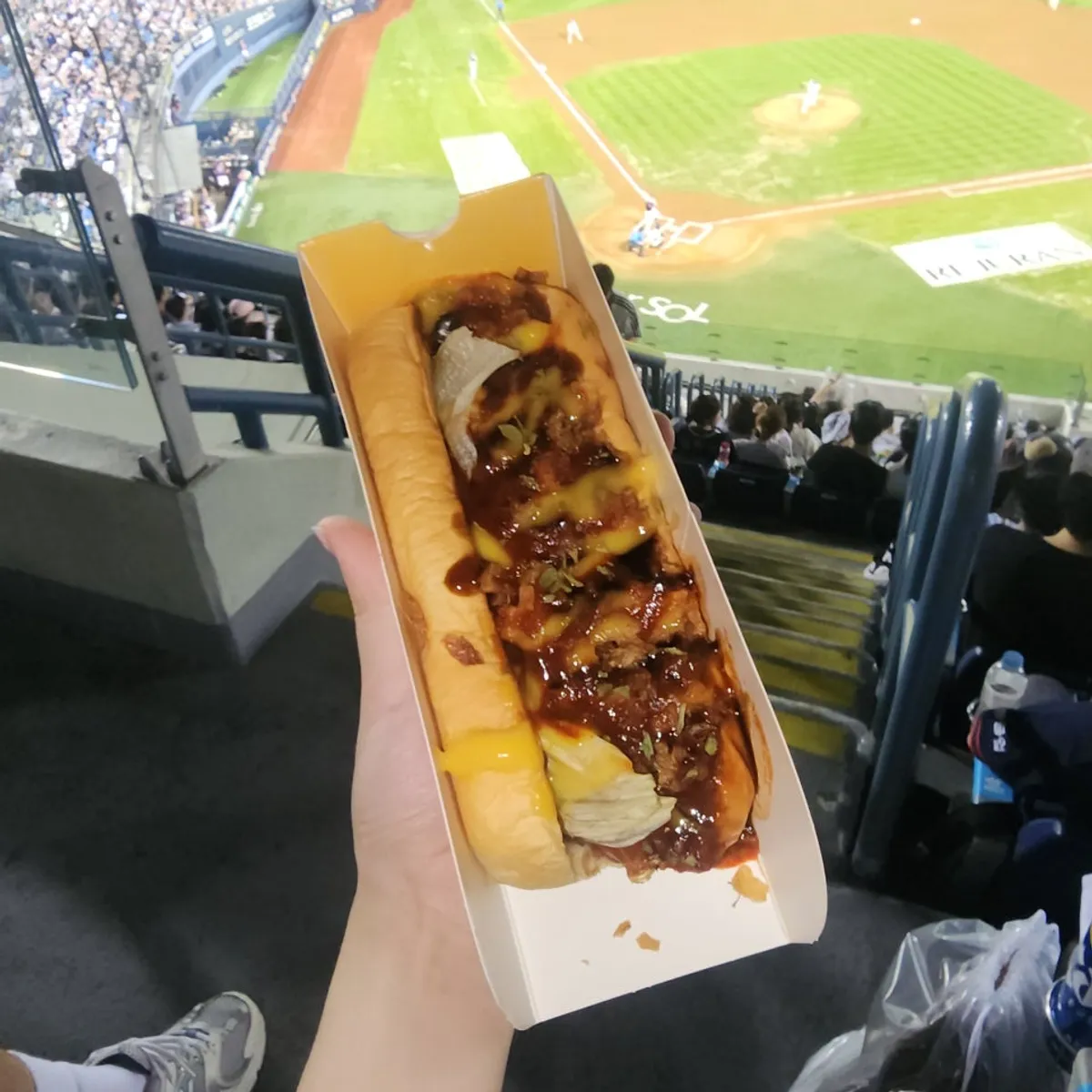 Chili cheese hot dog held in a stadium seat