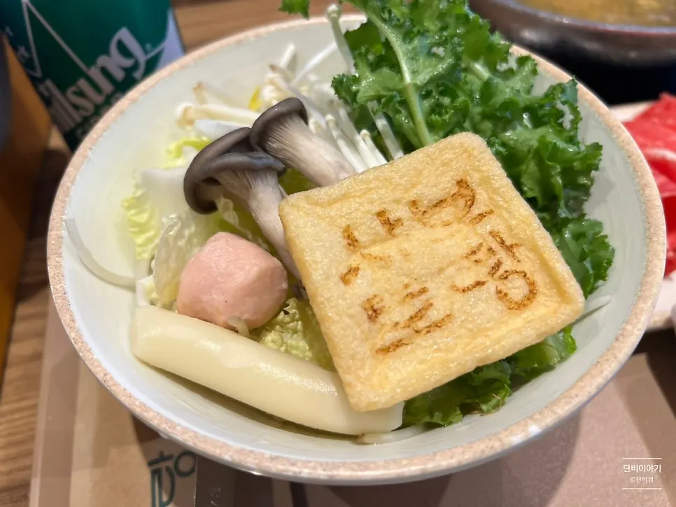 Square tofu pouch stamped with the Shabu Torang logo, with rice cakes and fish balls