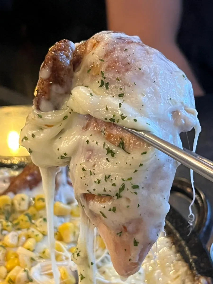 쭉 늘어나는 치즈를 올린 장작구이 통닭 한 조각