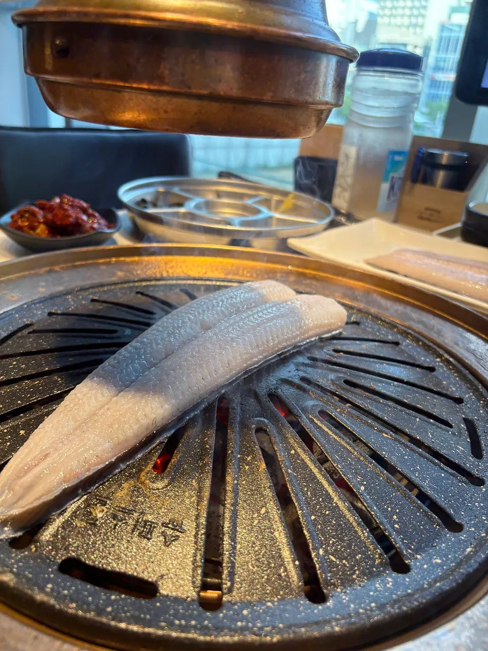 Beef grilling over charcoal with a drink on the side
