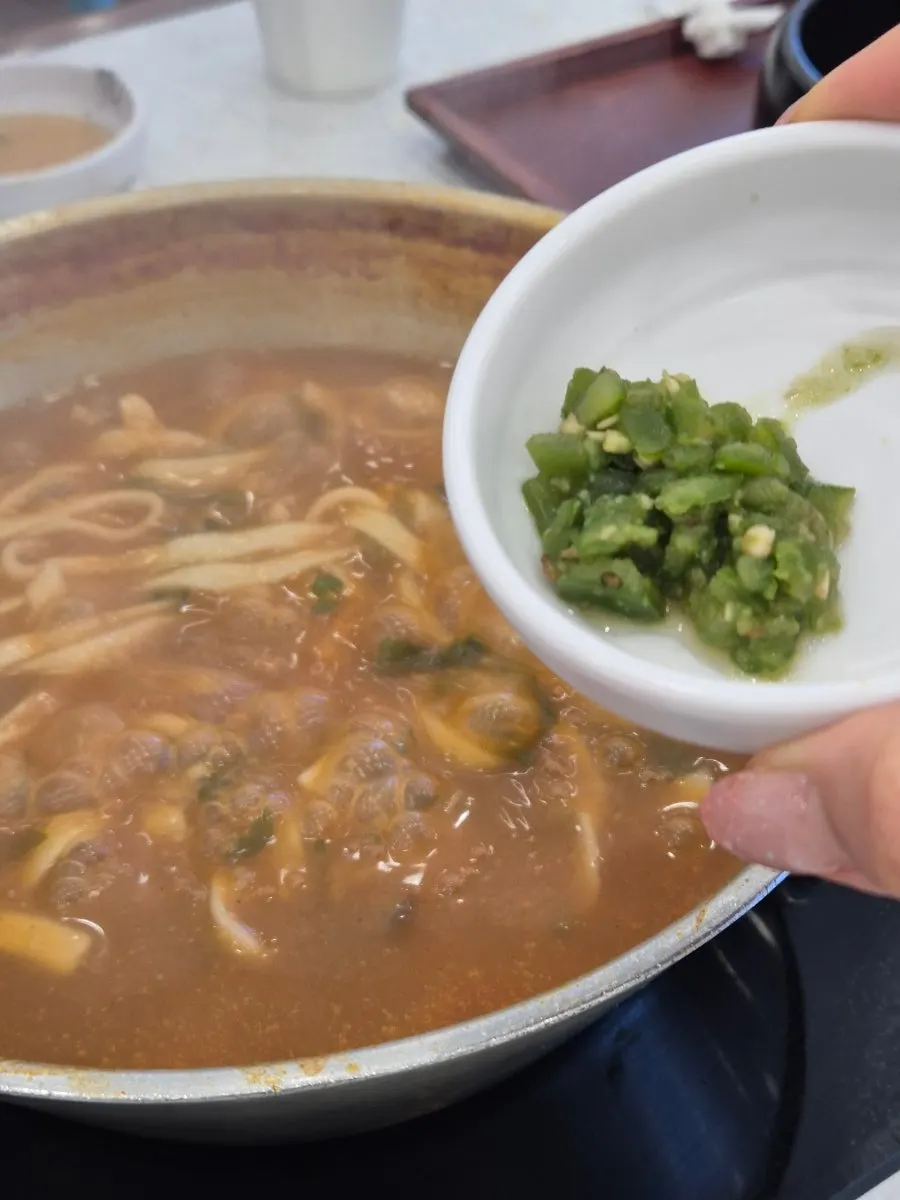 Kalguksu noodles cooking in boiling red broth