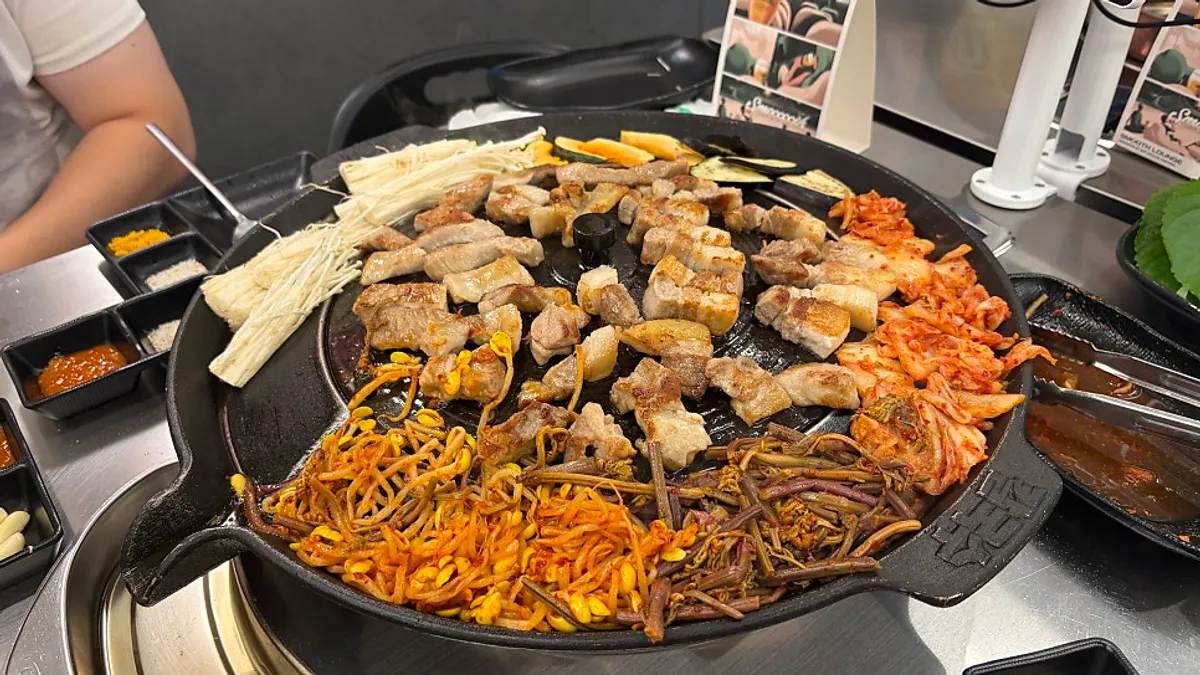 Pork belly grilling on the iron lid with attached side griddle