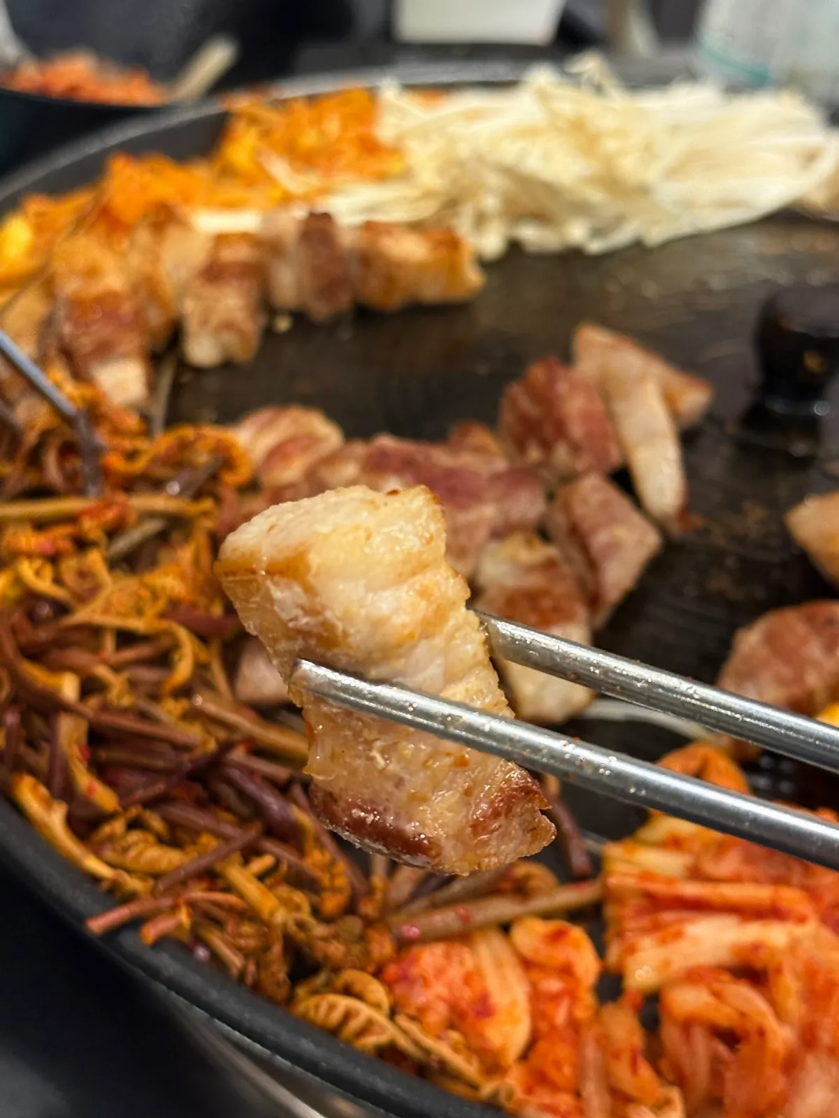 Pork belly grilling on the iron lid alongside kimchi and bean sprouts