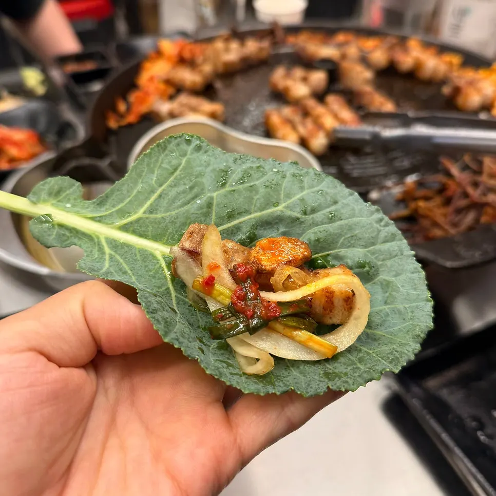 Bracken fern, kimchi, and bean sprouts grilling at the edge of the iron lid