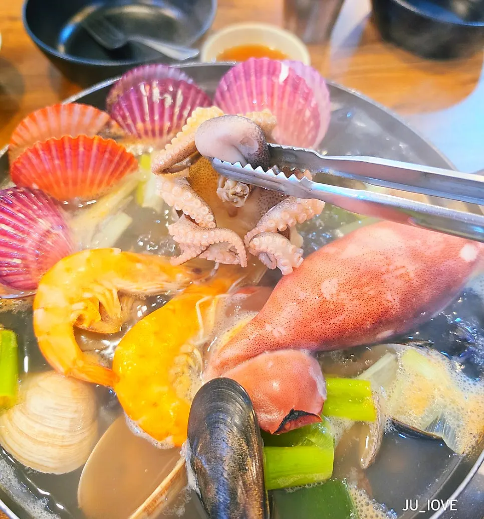 A ladle of clear broth drawn from the seafood