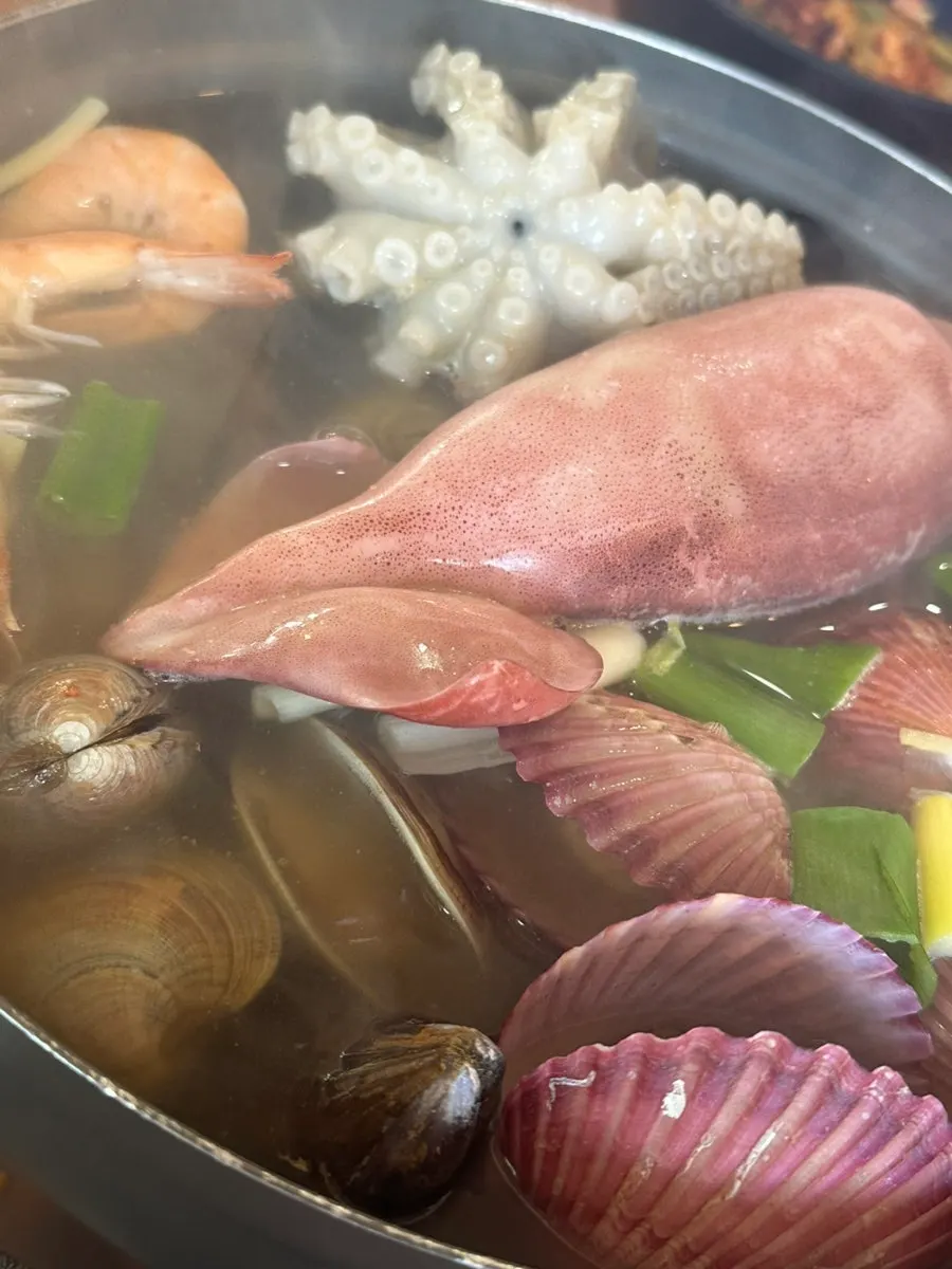 Pot of seafood kalguksu on the table with the how-to-eat guide