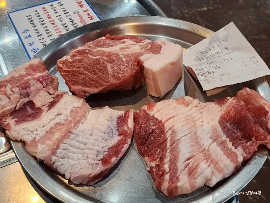 Black pork neck meat and raw pork ribs shown on a plate before grilling