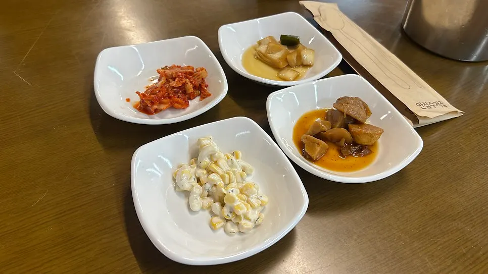 A spread of side dishes including kimchi, onion, corn salad, and sweet potato