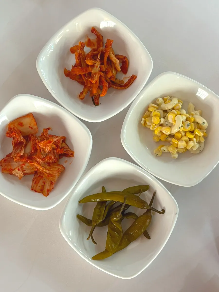 A spread of side dishes: corn salad, dried radish, kimchi, and pickled chili peppers