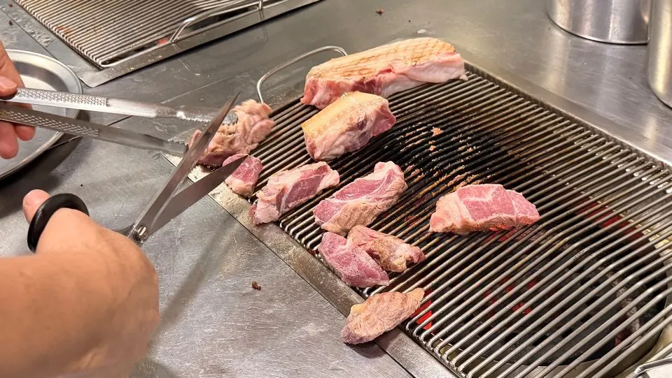 Staff member grilling black pork over charcoal