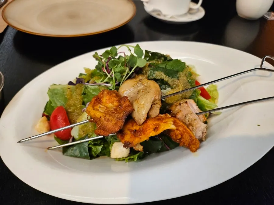 Salad plate topped with a tandoori chicken skewer