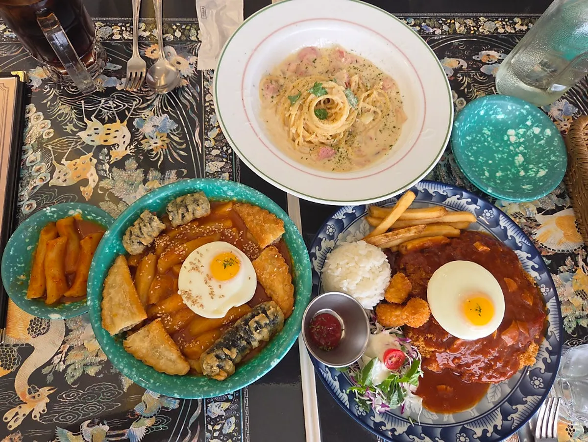 Overhead shot of cheese pork cutlet, bacon cream pasta, and tteokbokki