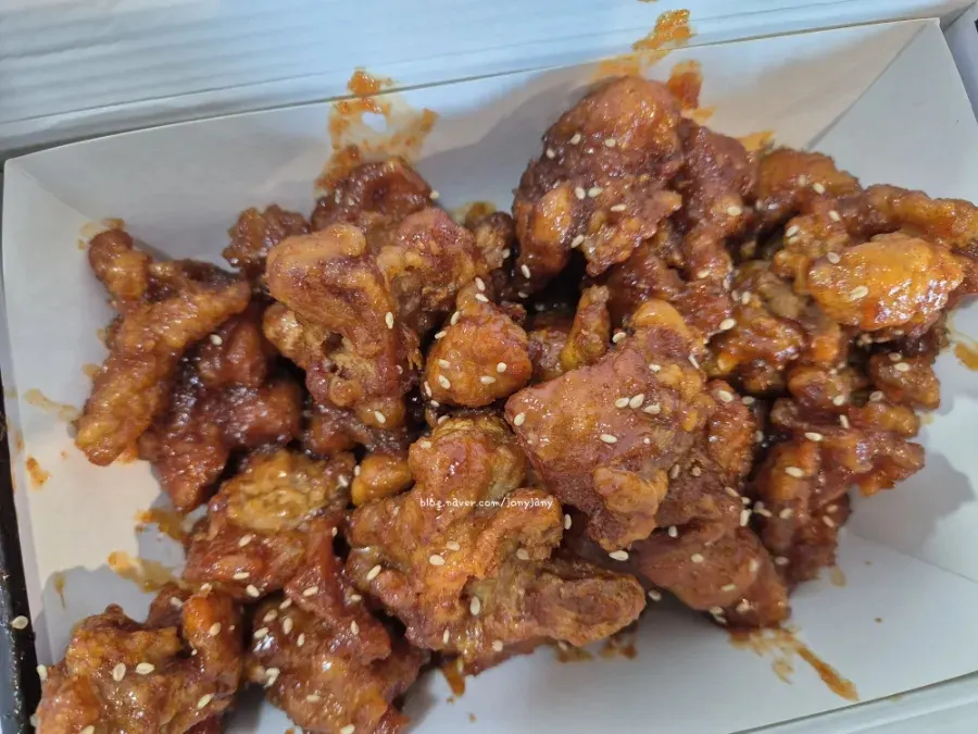 Takeout box full of sauced dakgangjeong sprinkled with sesame seeds