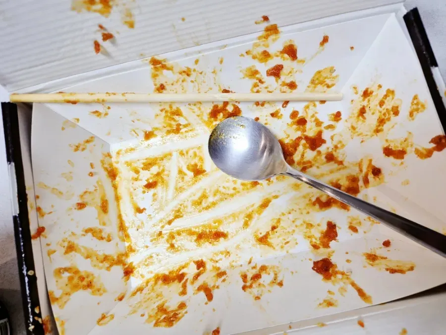 Boneless dakgangjeong dipped into leftover sauce at the bottom of the box