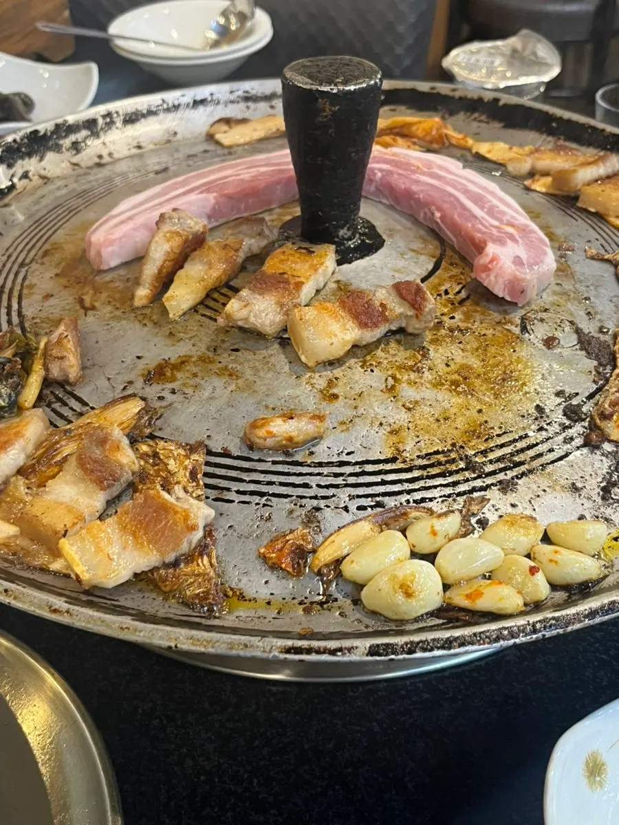 Meat and aged kimchi grilling together on the cast-iron lid