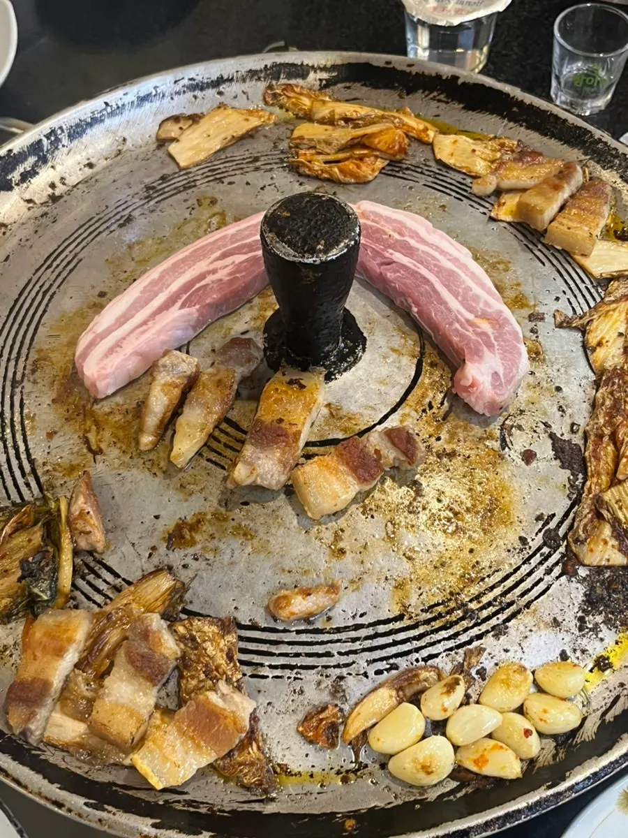 A bite of grilled pork belly topped with garlic and aged kimchi
