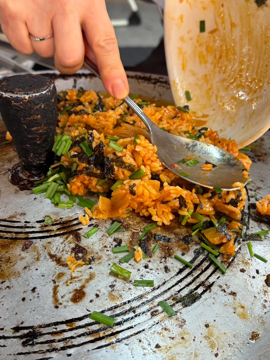 Kimchi fried rice spread out and stir-fried on the cast-iron lid