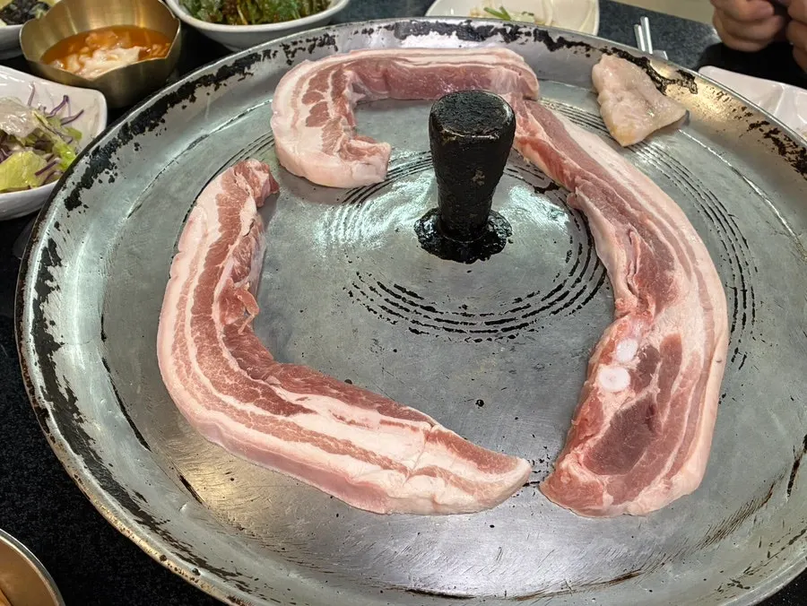 Raw pork belly placed on the cast-iron lid