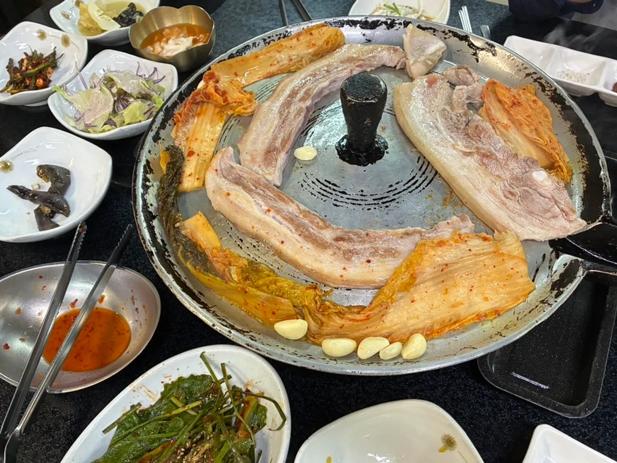 Pork belly grilling together with kimchi and garlic on the cast-iron lid