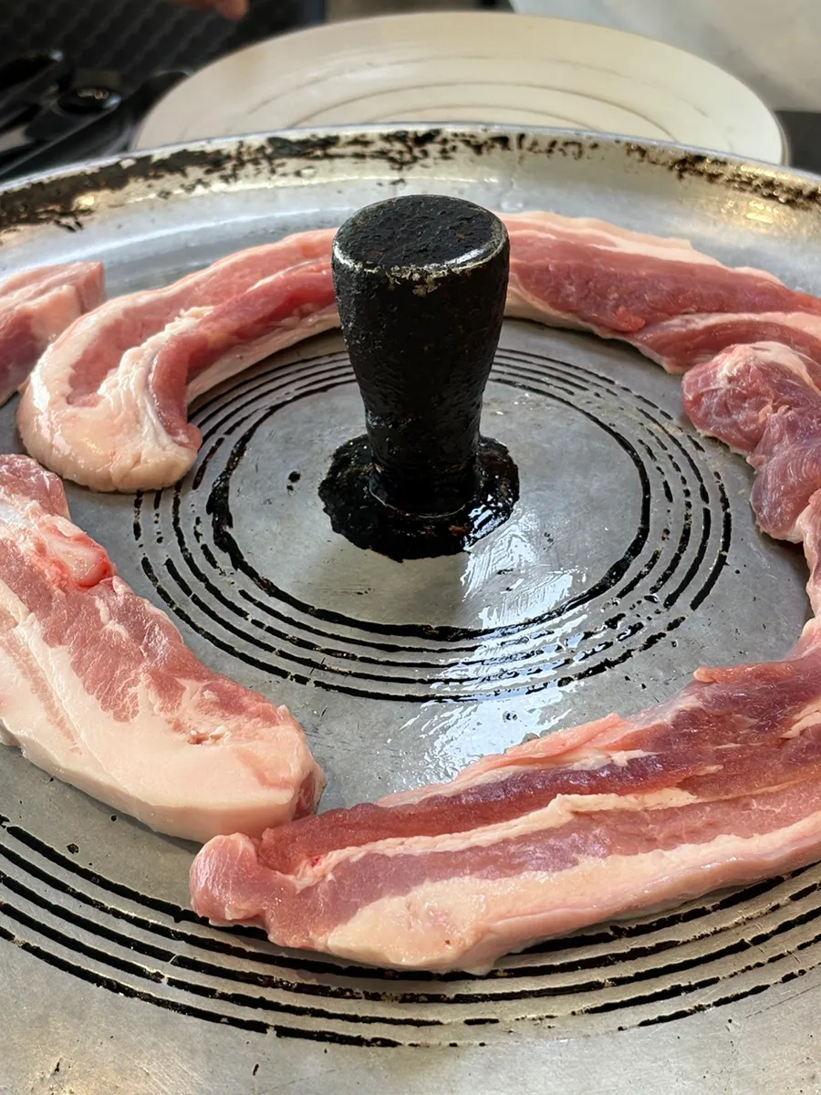 솥뚜껑에 올려 굽는 생삼겹살과 김치, 마늘