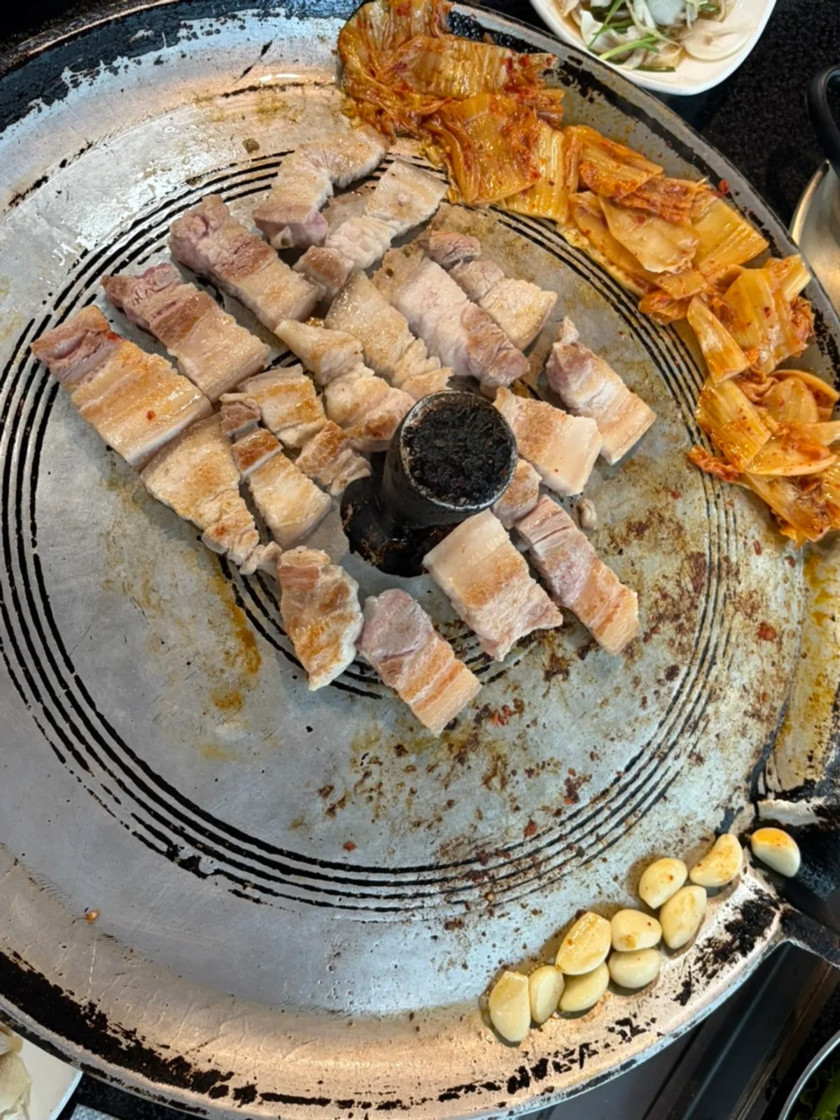 Cast-iron lid full of grilled pork belly and kimchi