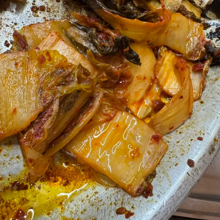 A slice of pork belly placed on top of aged kimchi