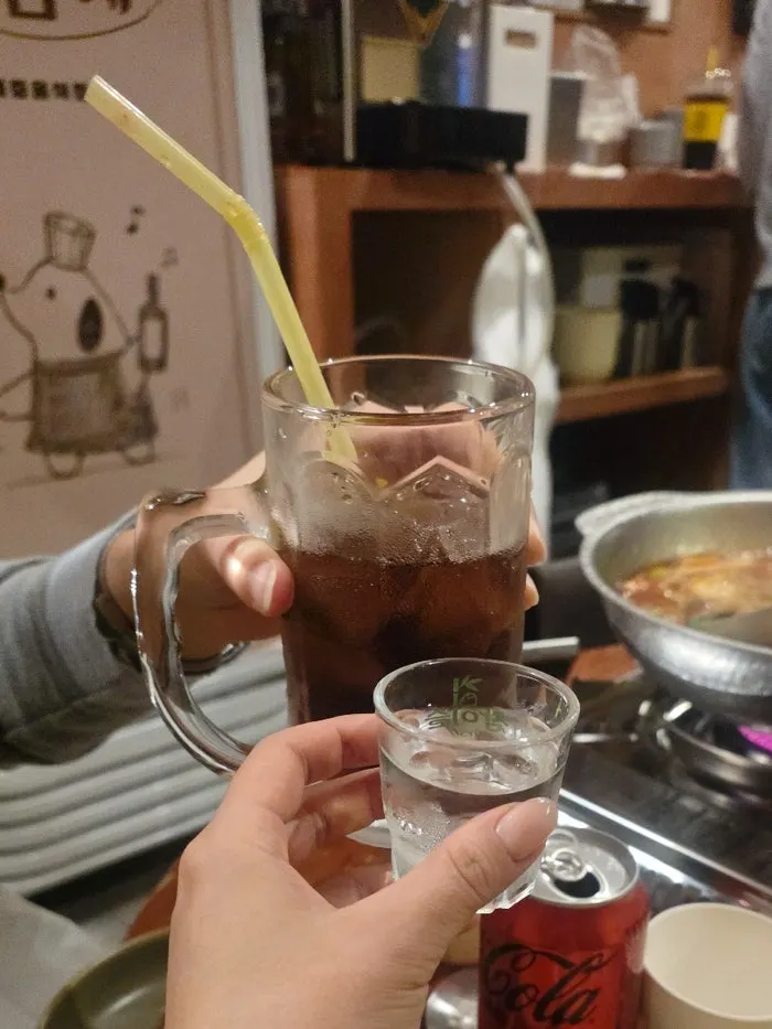 Table setting with zero-sugar cola and soju alongside the hotpot