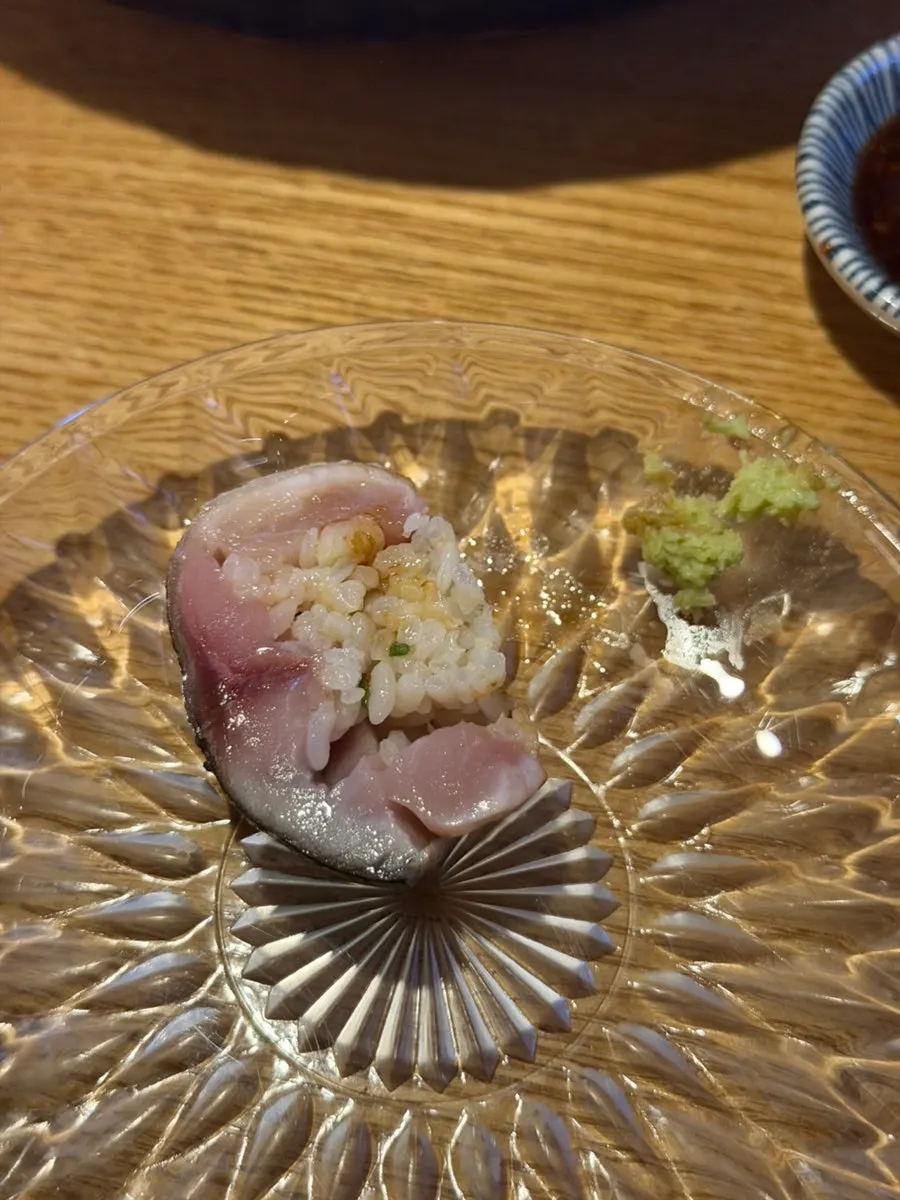 A piece of mackerel stick sushi topped with soy sauce and wasabi