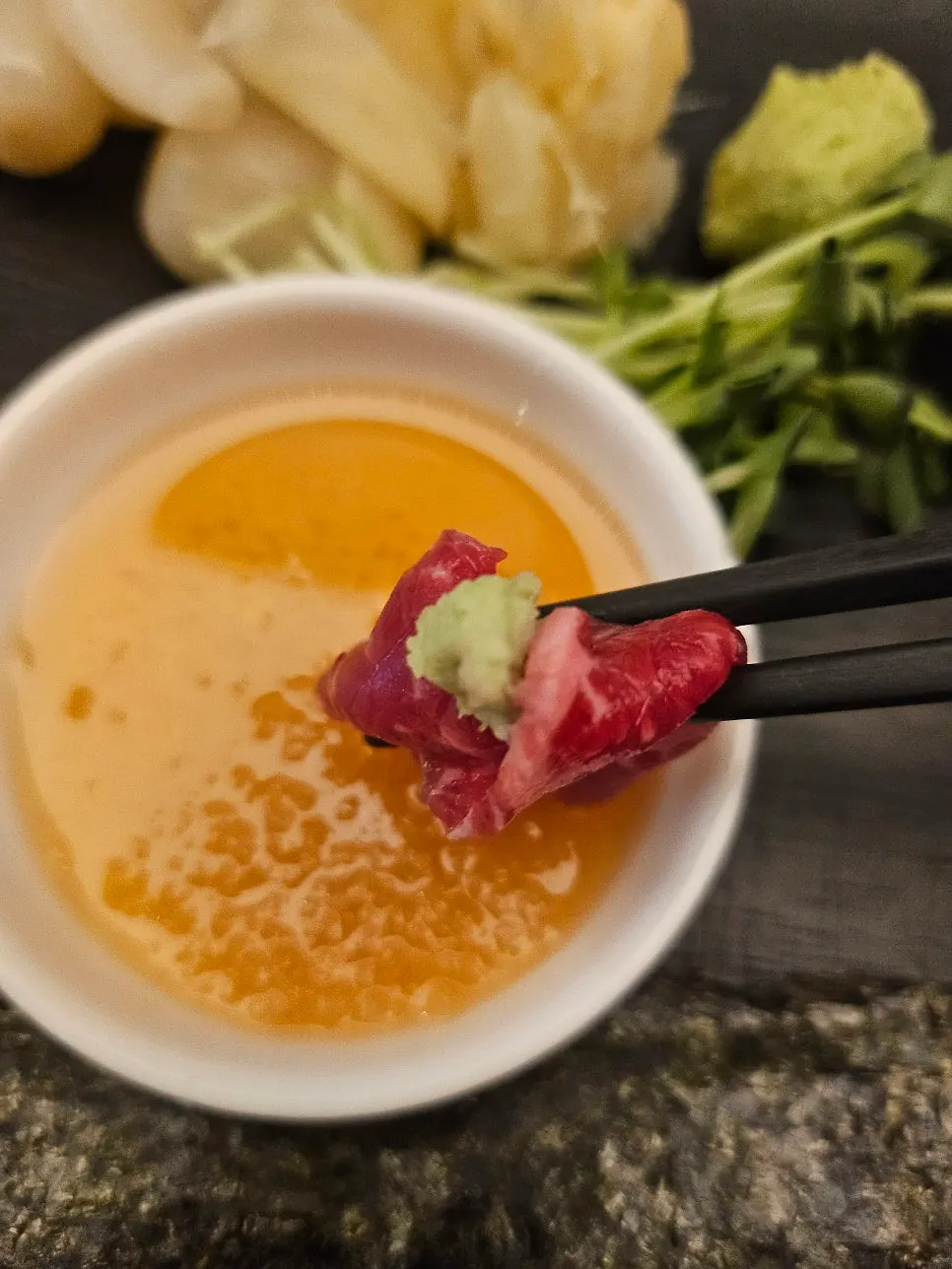 A piece of beef sashimi dipped in sesame oil sauce