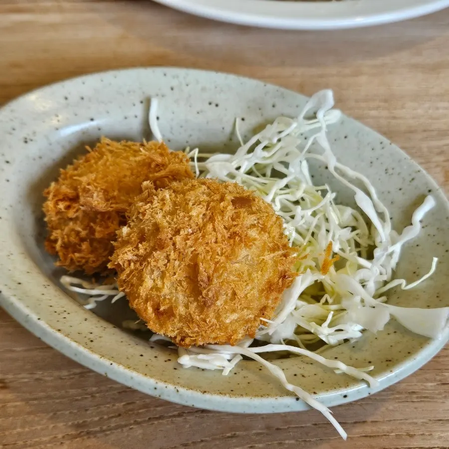 Two pieces of sweet potato cheese croquette on a bed of cabbage salad