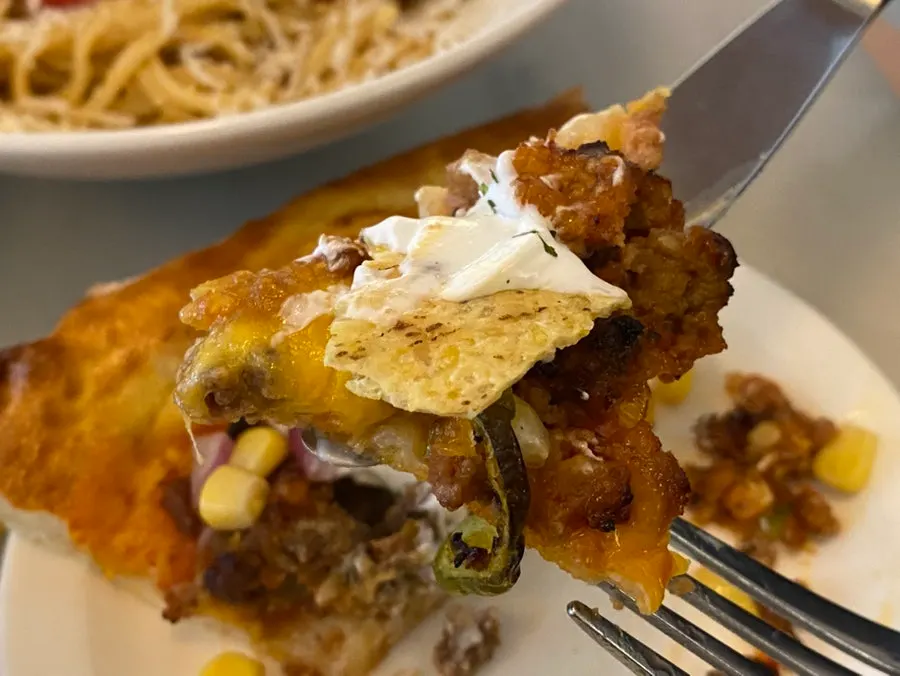 Cross-section of the taco pizza topped with sour cream and nachos