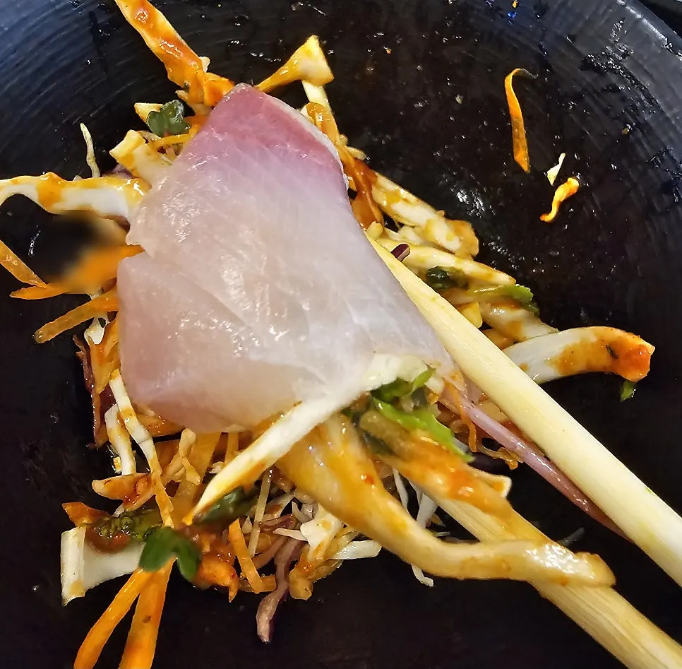 A piece of aged amberjack sashimi dipped in soy sauce