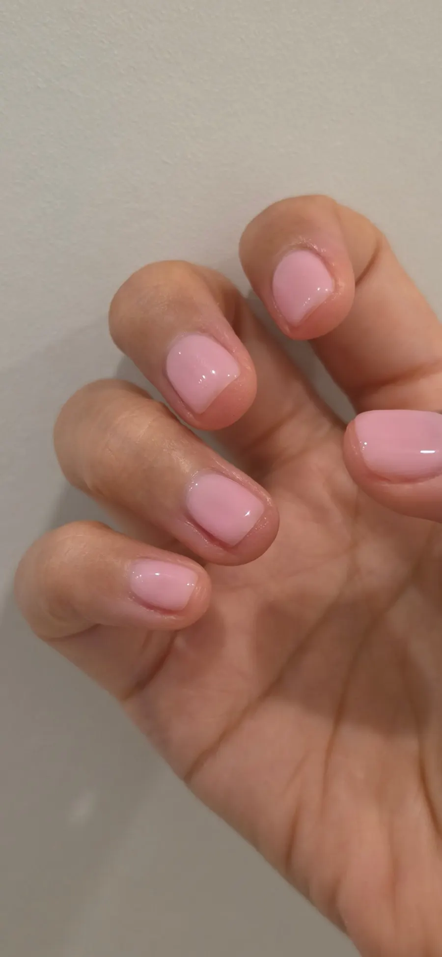 Hand photo of nudie pink gel nails under indoor lighting