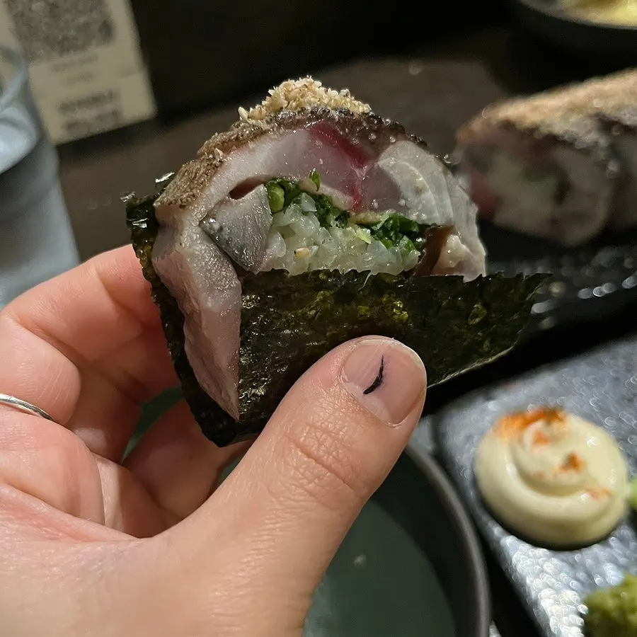Mackerel pressed sushi wrapped in seaweed and dipped in soy sauce