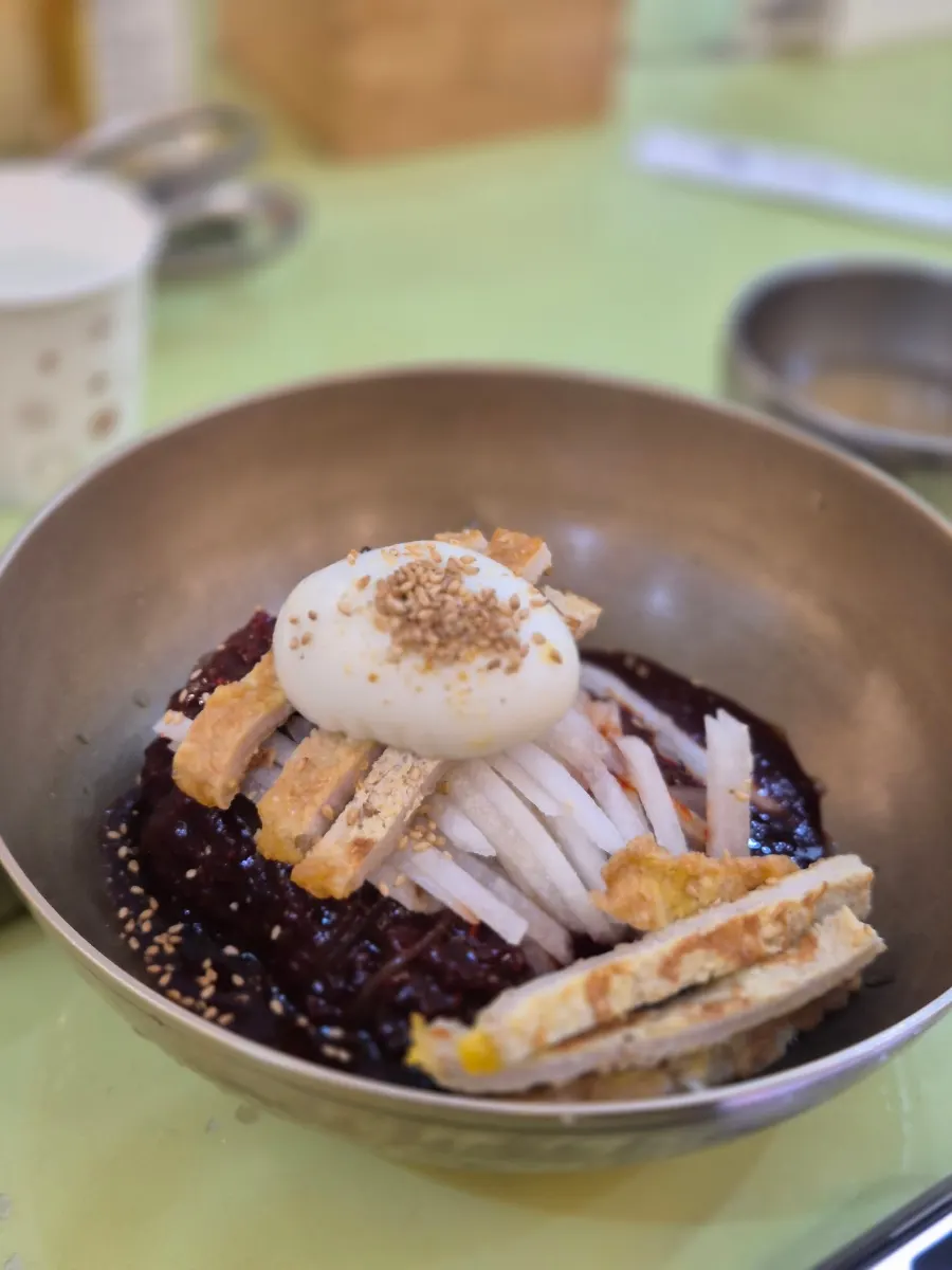 A bite of bibim naengmyeon topped with yukjeon