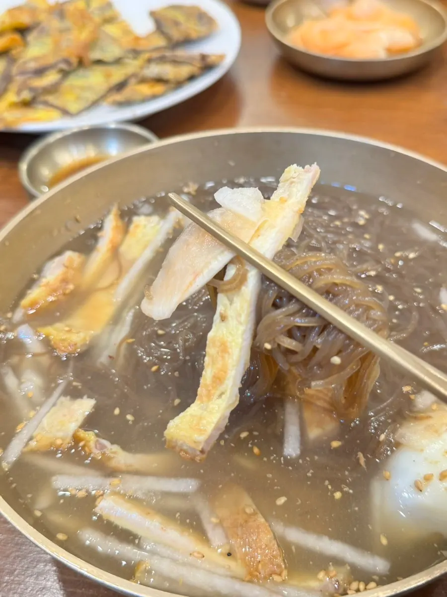 Water naengmyeon topped with yukjeon, egg, radish kimchi, and pear