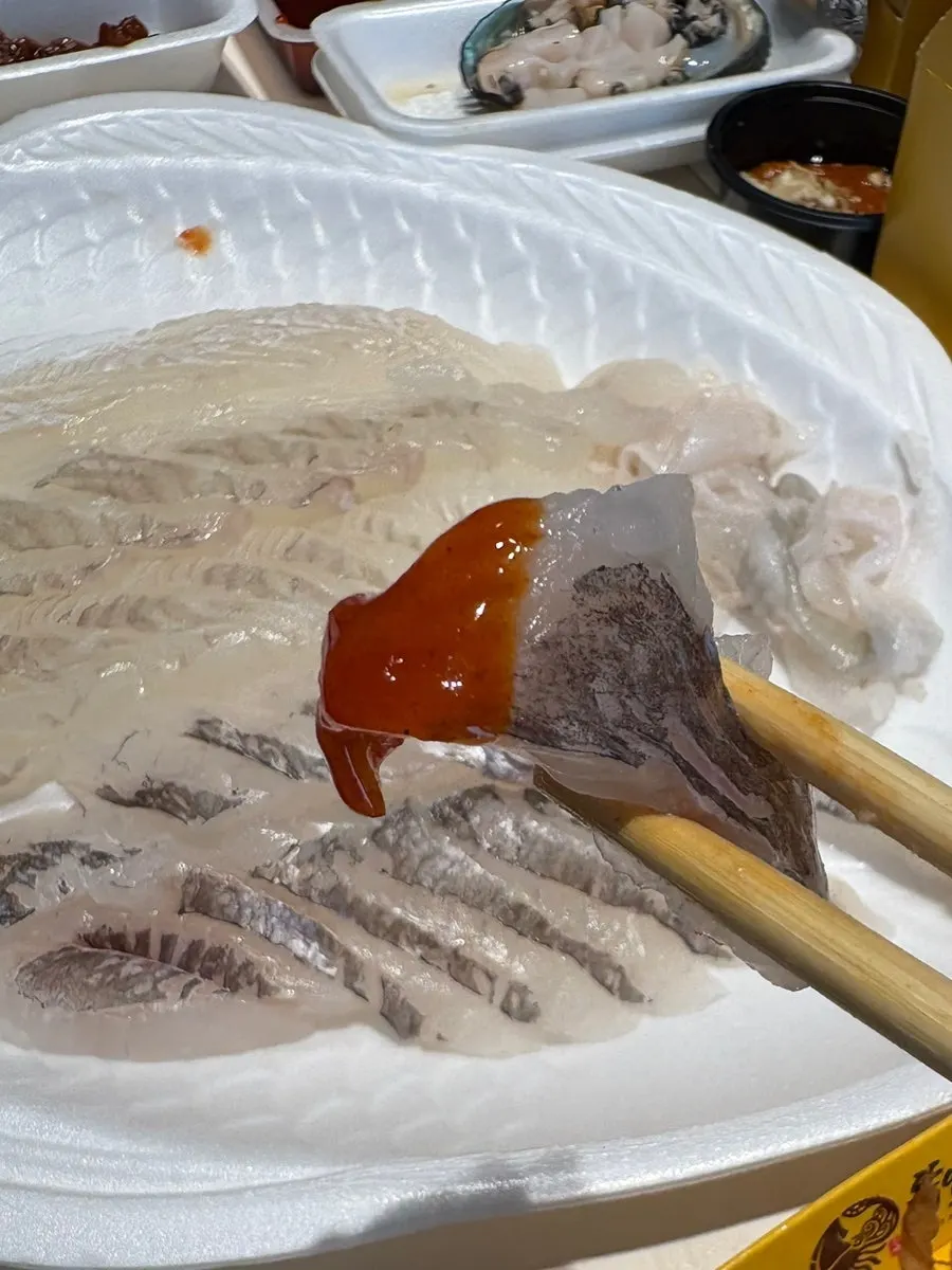 A piece of rockfish sashimi dipped in chojang sauce