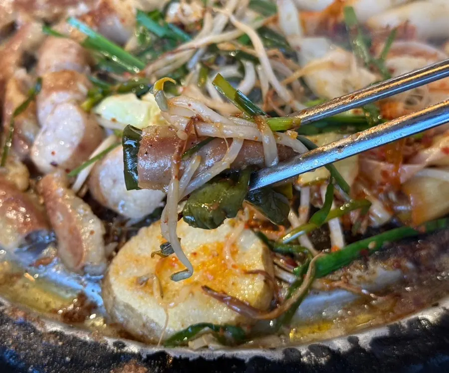 A piece of gopchang dipped in minari-garlic sauce