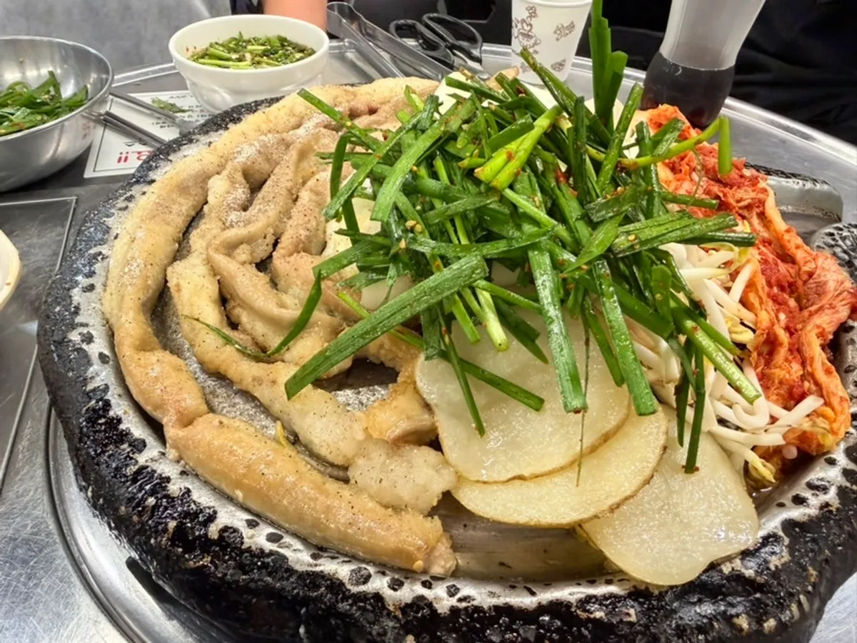 Grill piled high with chives, mung bean sprouts, potato, rice cakes, and kimchi alongside hanwoo gopchang