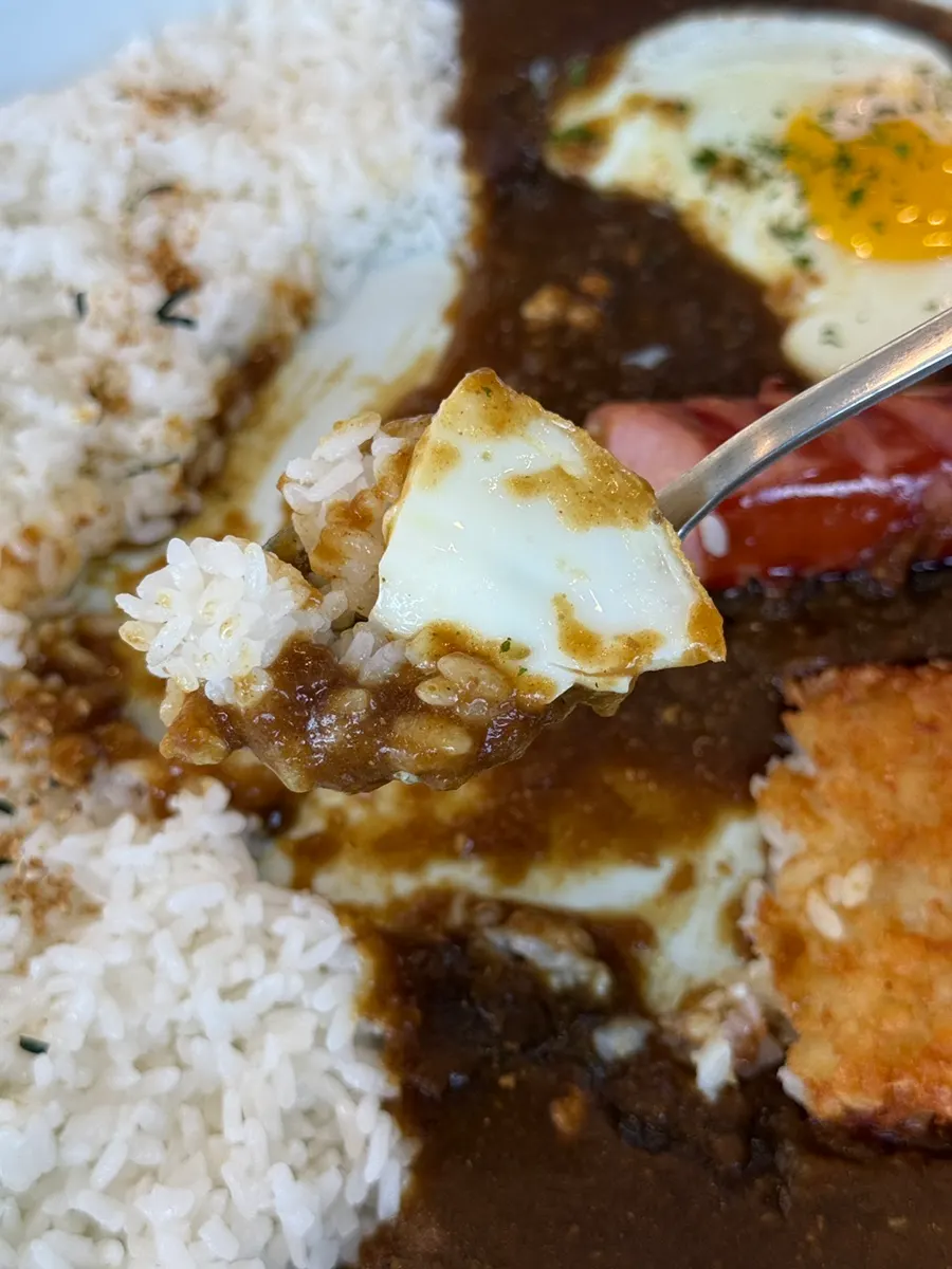 Curry rice bowl topped with fried egg, sausage and hash browns