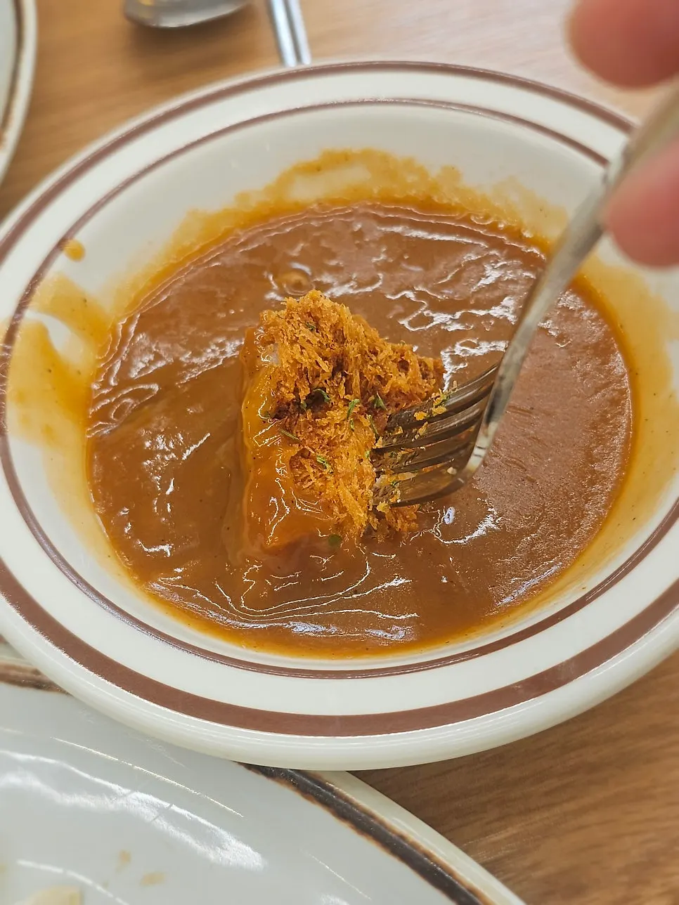 A piece of katsu dipped into the sauce bowl