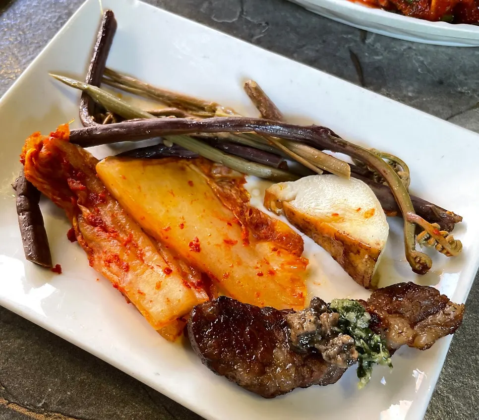 A piece of meat paired with grilled bracken fern and kimchi