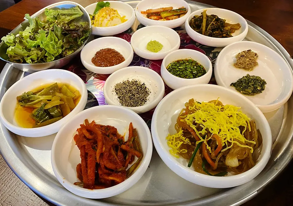 Full spread of Jipbul Taebaek banchan including japchae and green onion kimchi