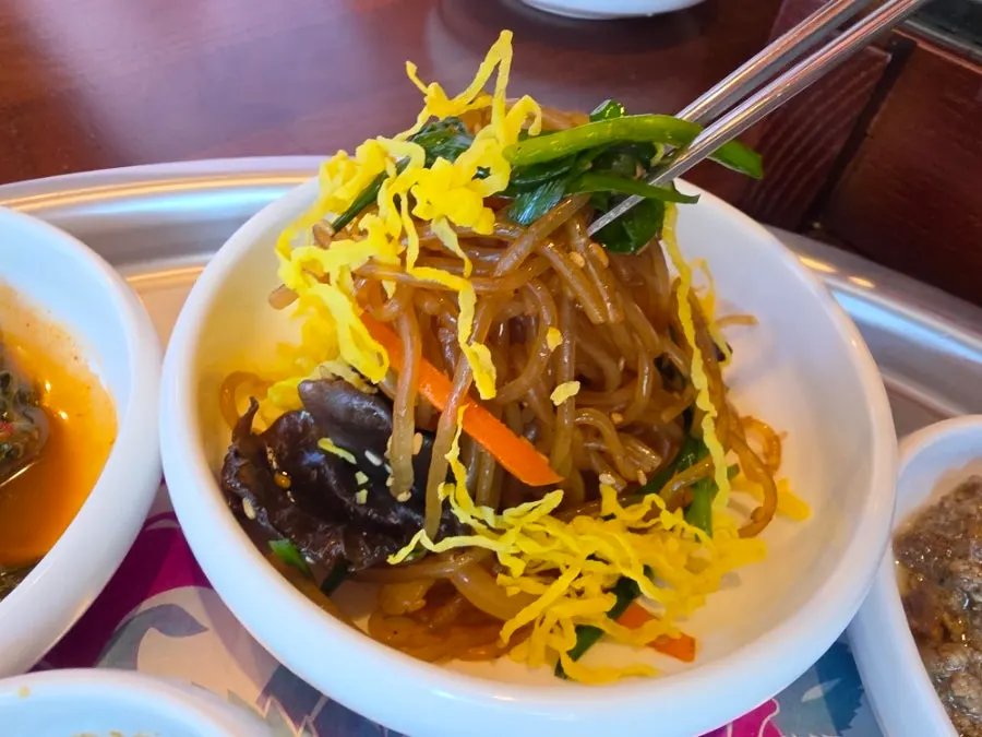 Side dishes including japchae topped with egg garnish