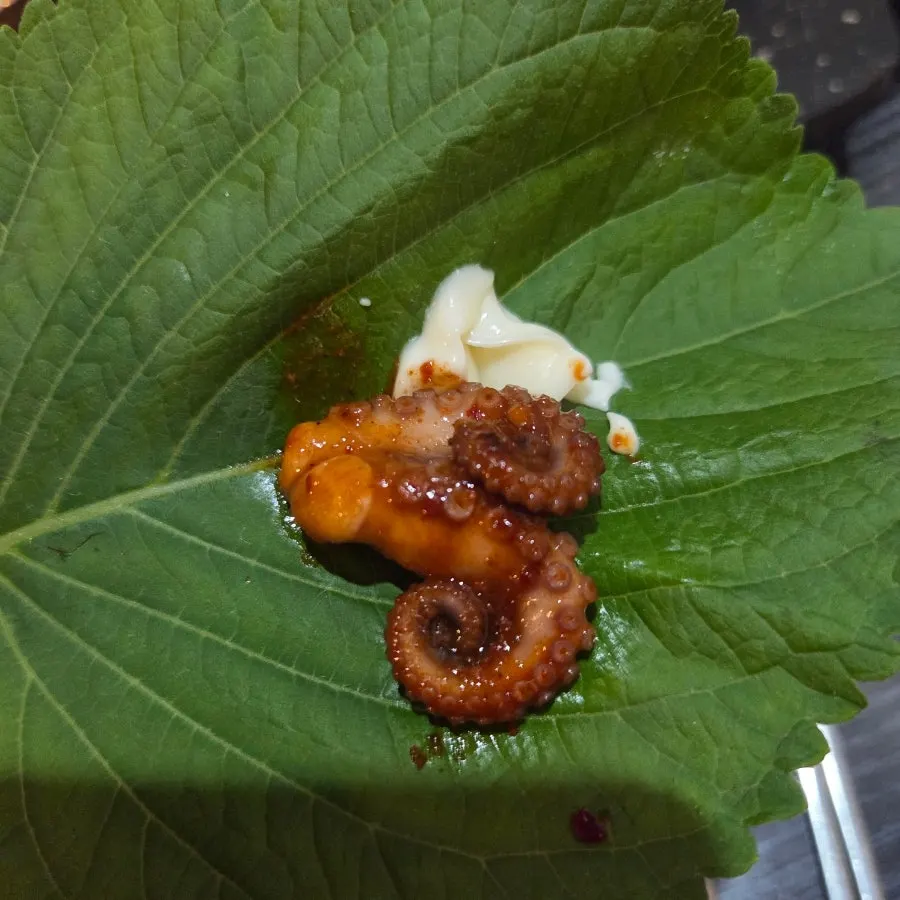 A bite of octopus on perilla leaf with mayo