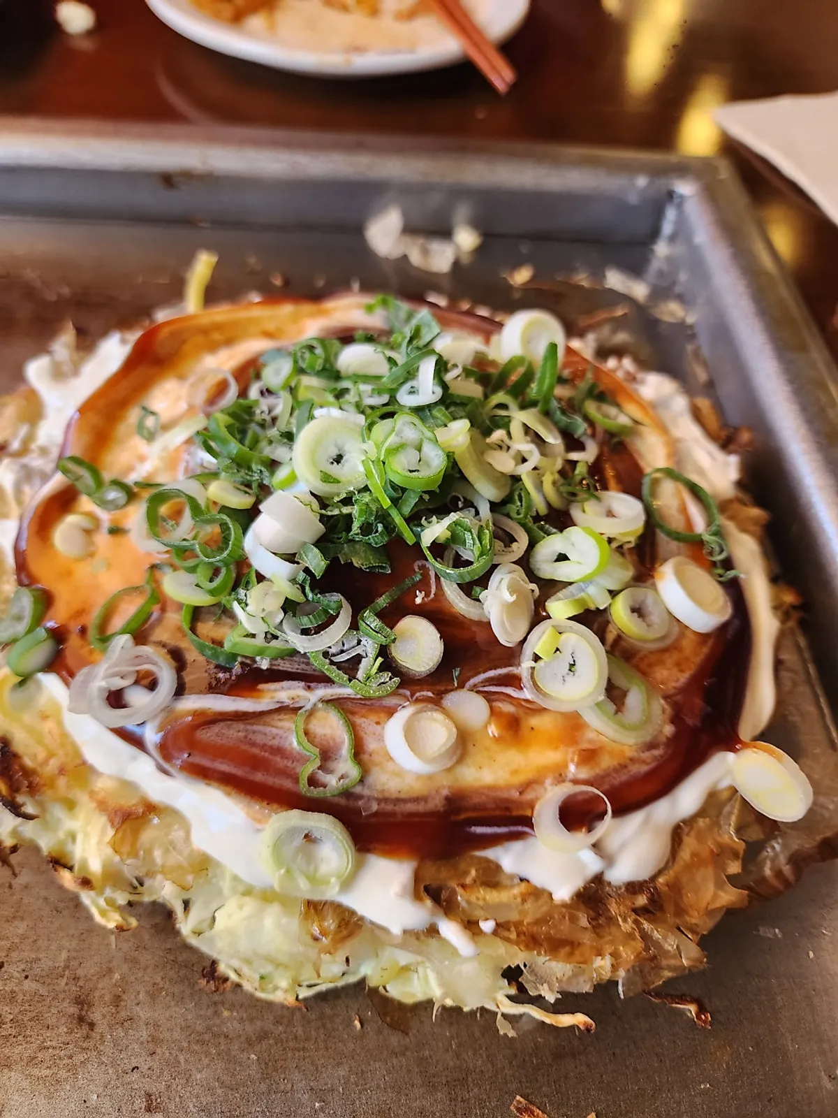 Finished Jojo okonomiyaki piled high with scallion garnish