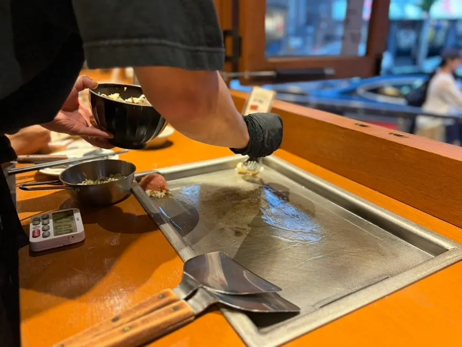 Staff member cooking monjayaki on the tabletop griddle